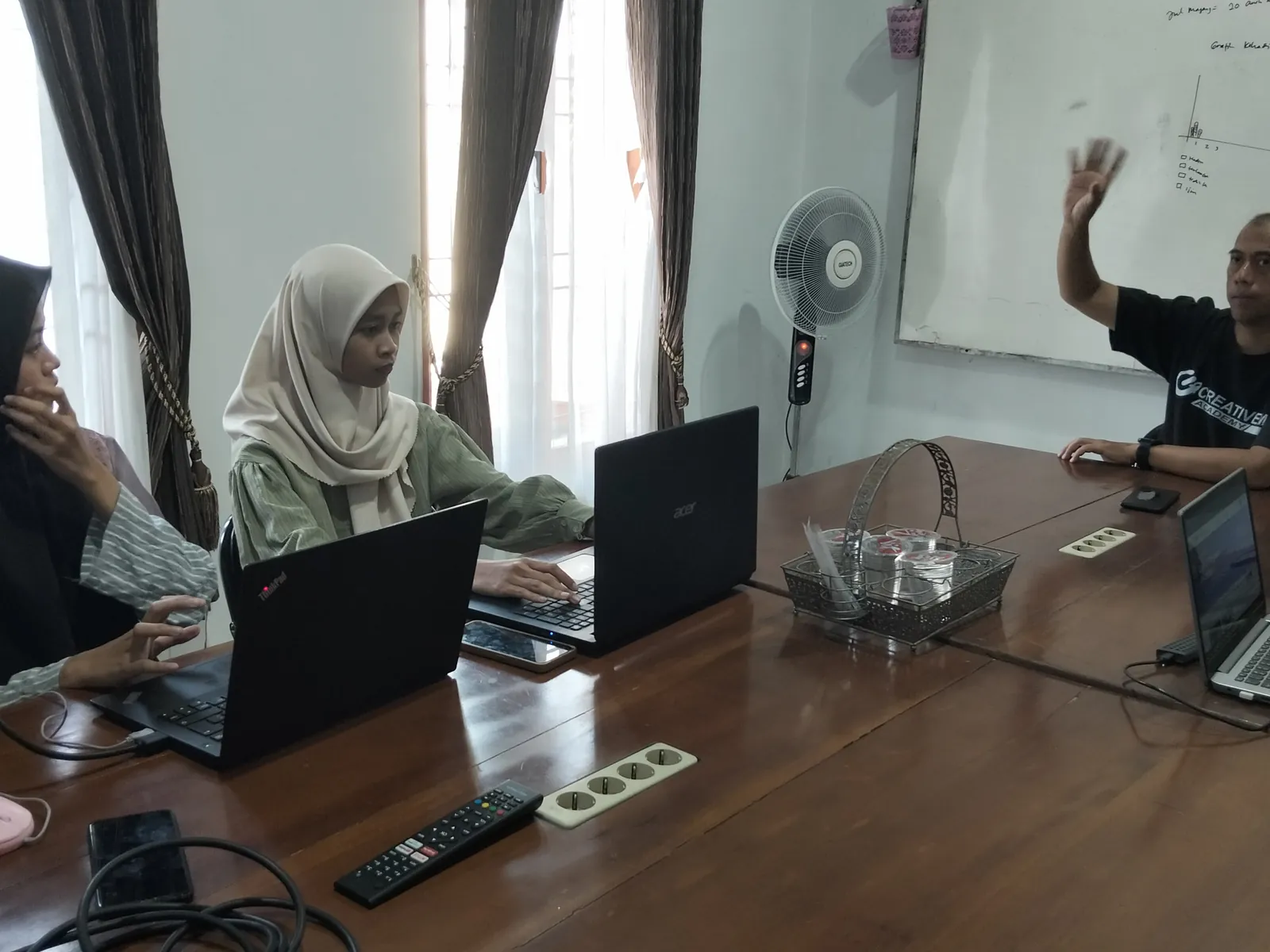 Mentor mengangkat tangan menjelaskan materi kepada peserta di ruang kerja